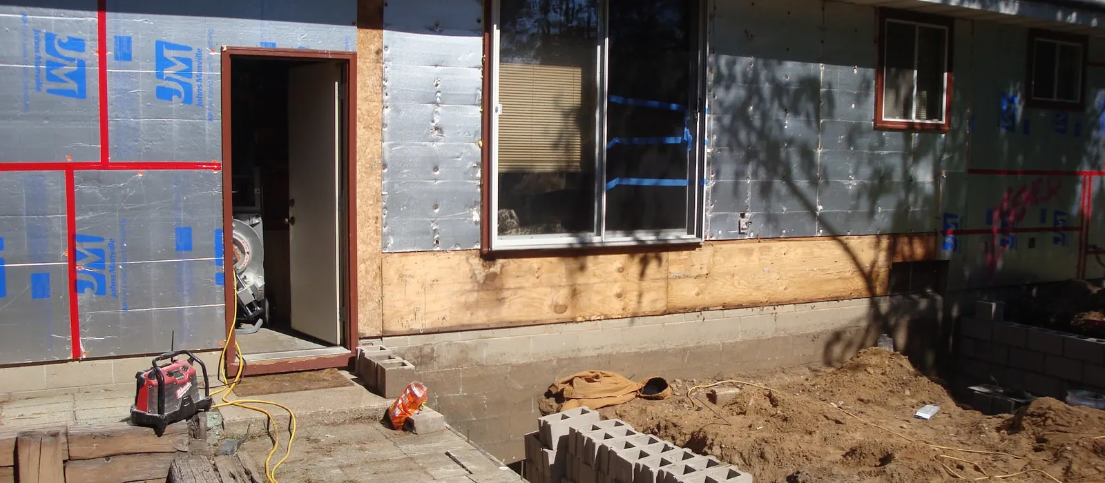 A ranch house stripped to sheathing, with new block courses and stone laid at grade.