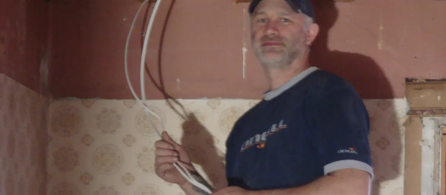 White NM cable being fed through an opened wall in a stripped room.