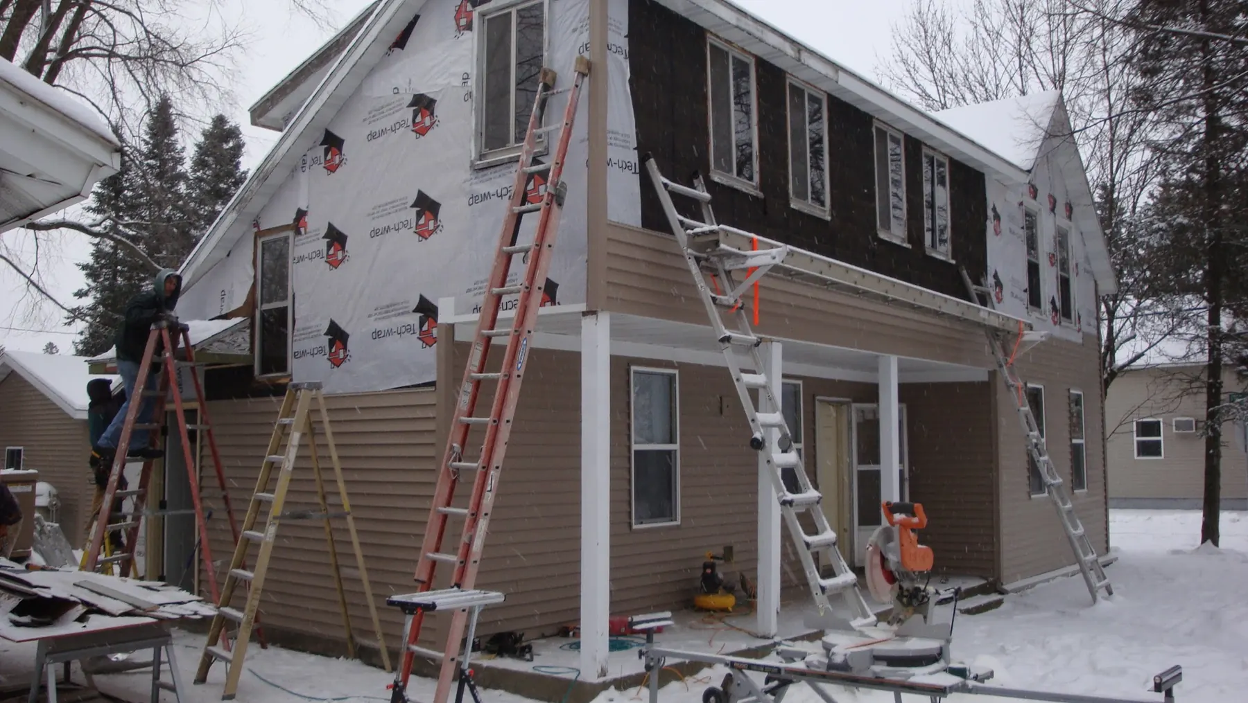 A two-storey Stevens Point house mid-re-side, five red extension ladders leaning across the elevation and snow on the ground.